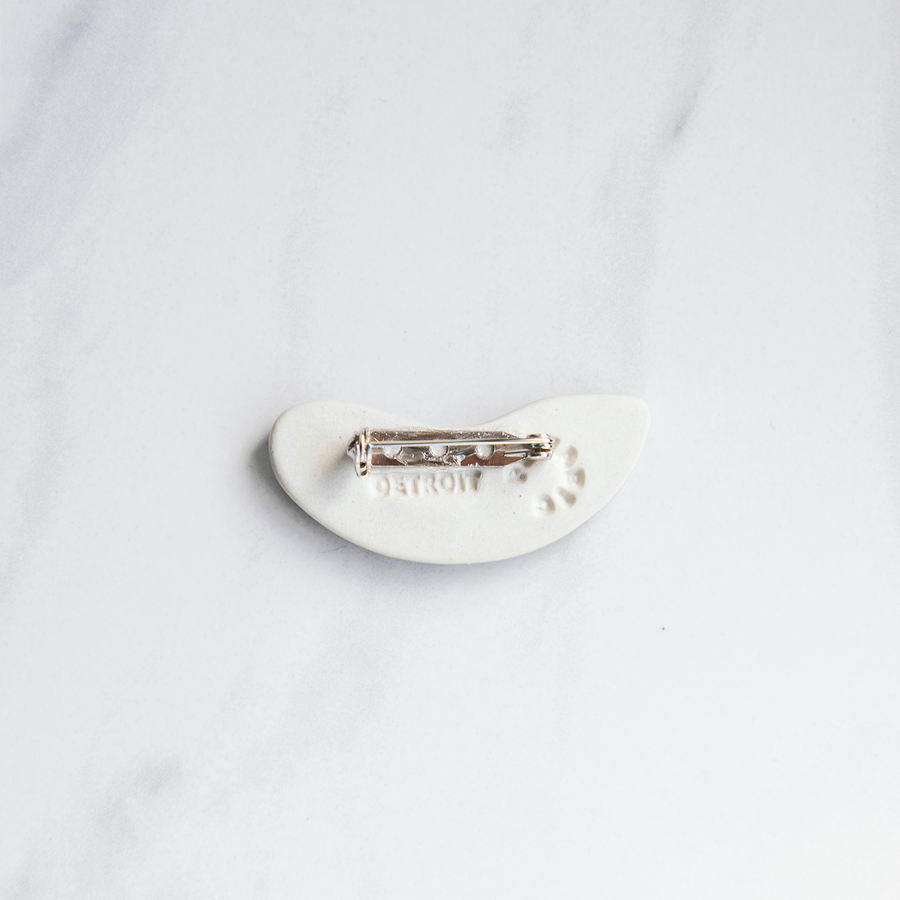 The back of the pin is bright white porcelain and features a "Detroit" stamp and a round, Pewabic logo stamp. The silver pin-back is glued onto the tiny pin tile.