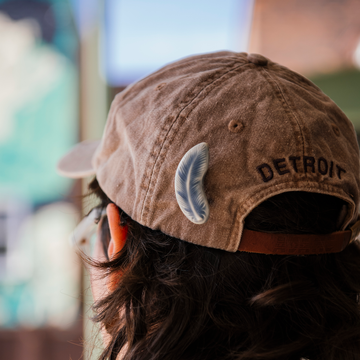 This Feather is pinned onto the back of a dusty mauve colored baseball cap. 