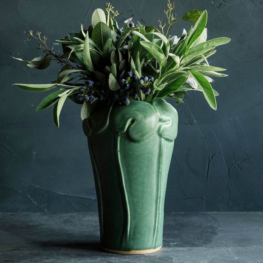 The Lotus Vase features a tall base with long stalks reaching up to a ring of lily pads that crown the top and lip of the vase.