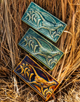 Three Pheasant tiles rest on a bed of brown grasses. The tiles are in each glaze option - Kale, Glacier Gloss and Molasses.