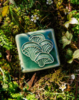 The Oyster Mushroom tile features a clump of four oyster mushrooms stacked on top of each other. Each mushroom has a smooth cap and gills that run the length of its stem.