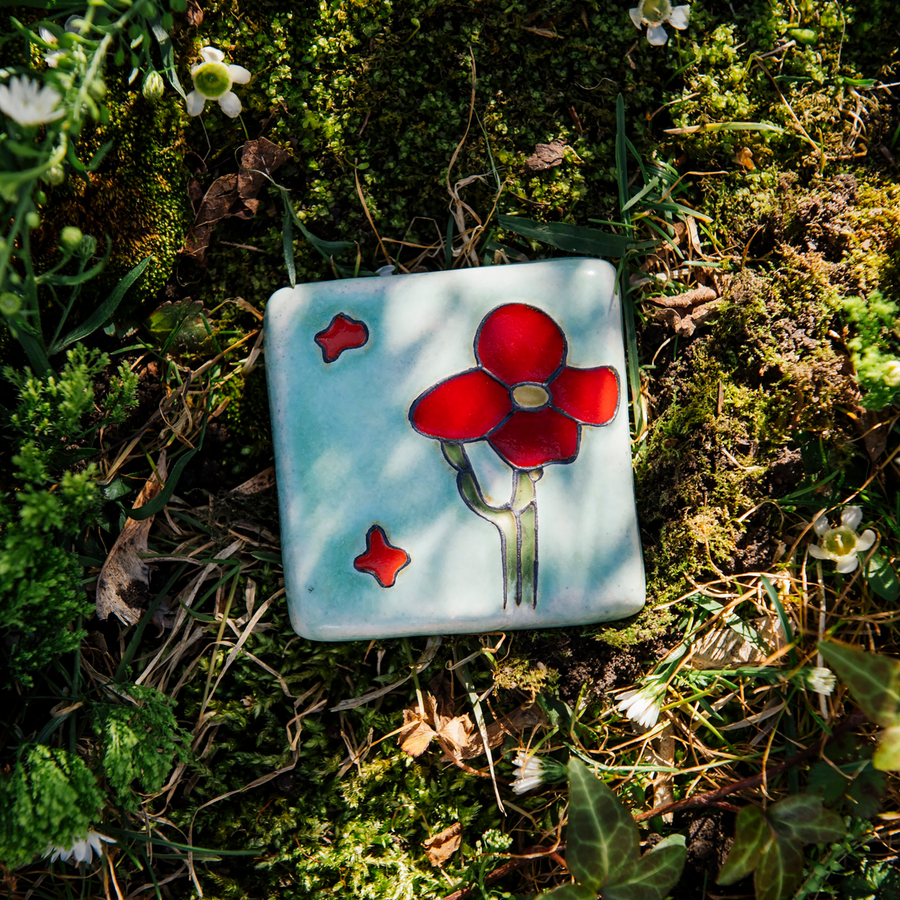 The handpainted tile in the Poppy Palette features bight red petals and a medium green cactus stem. The background of the tile is a pale blue color.