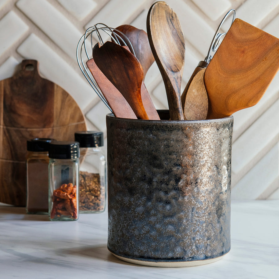 This Pewabic Crock sits on a white marble kitchen counter. The crock features the metallic gray textured Graphite glaze and holds wooden cooking utensils.