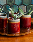 Four Pewabic Rocks Cups in our glossy-red Winterberry glaze on a copper tray with cranberries and sage. 