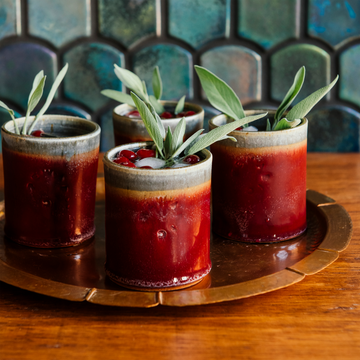 Four Pewabic Rocks Cups in our glossy-red Winterberry glaze on a copper tray with cranberries and sage. 