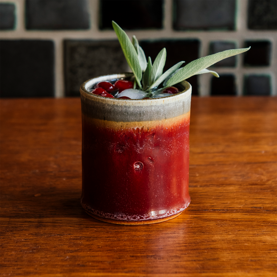 One Pewabic Rocks Cups in our glossy-red Winterberry glaze on a wood foreground with cranberries and sage.