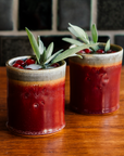 Two Pewabic Rocks Cups in our glossy-red Winterberry glaze on a copper tray with cranberries and sage. 