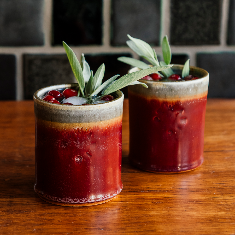 Two Pewabic Rocks Cups in our glossy-red Winterberry glaze on a copper tray with cranberries and sage. 