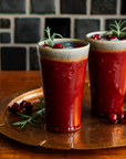 Two Pewabic Pints in our glossy-red Winterberry glaze on a copper tray with cranberries and rosemary. 