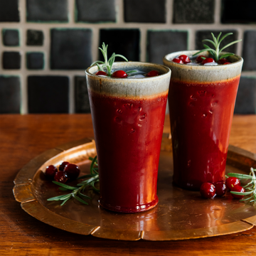 Two Pewabic Pints in our glossy-red Winterberry glaze on a copper tray with cranberries and rosemary. 