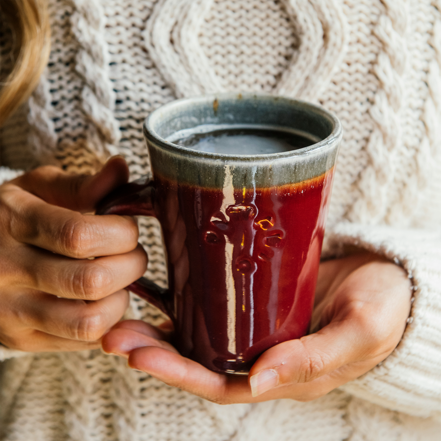 This Cafe Mug is being held by a woman in a cozy, creme-colored sweater. The base of the mug is resting in her hands.