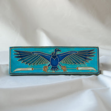 The short and wide Nekhbet tile features a line drawing of a vulture with wings outstretched, head turned to the right as she holds two stylized feathers- one in each talon. This tile features bright shades of blue.