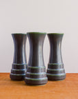 Three Step Vases in the Gun Metal Glaze sit together on a wood table. Each has slightly different amounts of the green lightening on the steps of the vase.