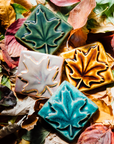 All four colors of the maple leaf embossed tile are resting on a bed of fall leaves. Each maple leaf design covers the entire surface of the tile. 