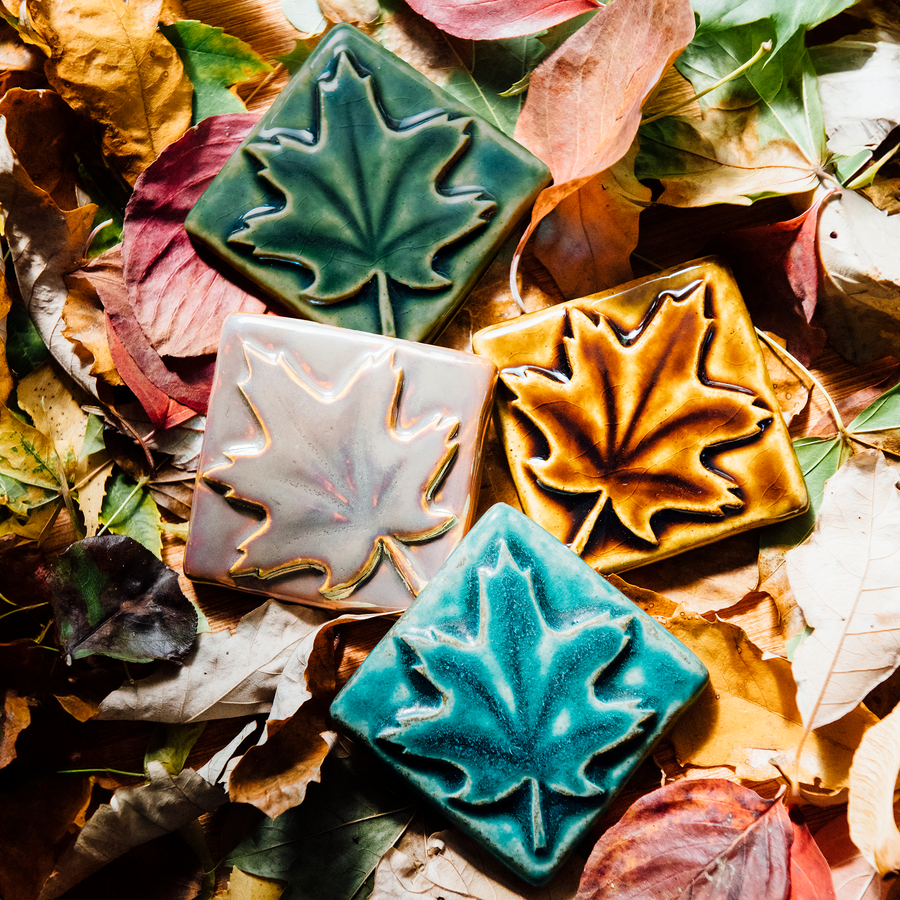 All four colors of the maple leaf embossed tile are resting on a bed of fall leaves. Each maple leaf design covers the entire surface of the tile. 