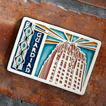 The Guardian Building Tile design features the top of the building on the right side of the tile with the word "Guardian" on the left. A large version of the Pewabic tiles found on the Guardian Building are framing the left side of the image. The tile is hand-painted in blues with red and yellow accents.