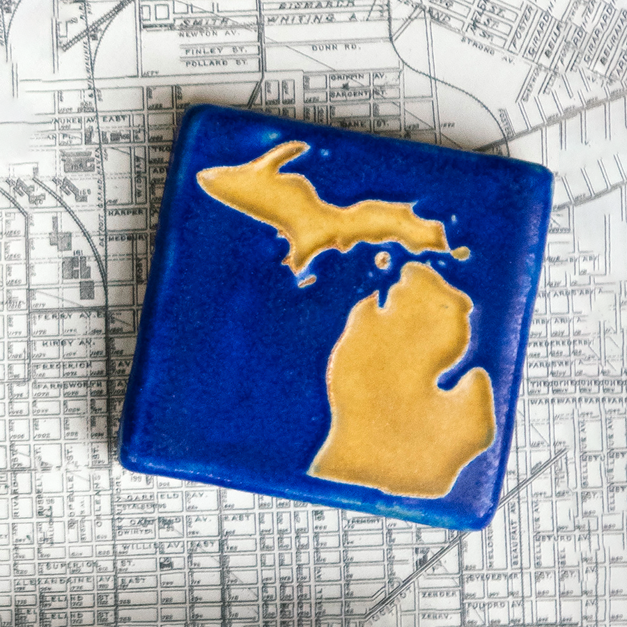 The Michigan Outline Tile features the outline of the state of Michigan with both peninsulas and its larger northern islands. This hand painted tile has a background of deep matte blue while the peninsulas are a maize gold color.