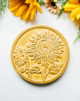 The Sunflower Trivet Tile features two sunflowers growing up into the circular tile with leaves and a bit of stalk in view. One sunflower is facing forward while the other is slightly smaller and facing to the left.