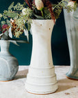 A Birch Step Vase sits among glossy pale blue Frost glazed pieces. They compliment each other well.