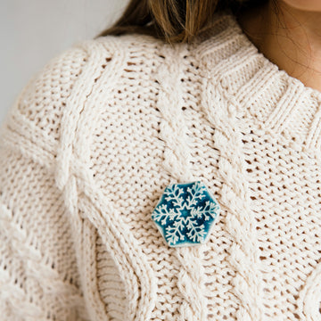 This delicate Snowflake Pin is a hexagonal shape. Six frosted tines break out from the snowflake's center. The pin in glaze in a glossy blue color that is almost white on the raised snowflake design and pools to a deep color on the background. 
