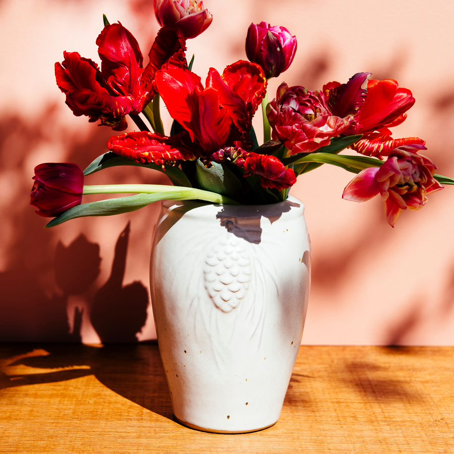 The Pinecone vase features smooth sides with three high relief pinecones and pine needles near the lip of the vessel. Each pinecone points in a different direction so there is always one pinecone pointed outward no matter which direction the vase is sitting. The top of the vase has a simple raised lip that come in toward the center.