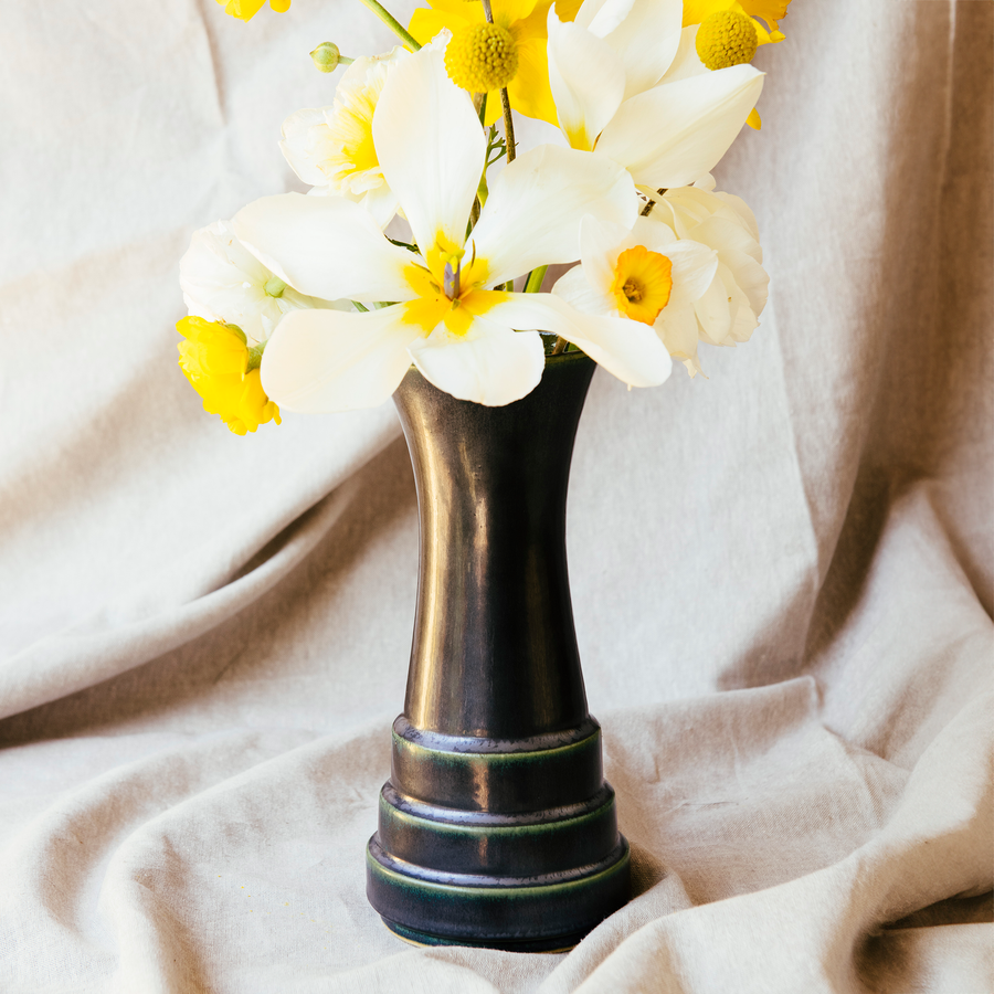 This Step Vase features the satin-finished steel black Gun Metal Glaze. In areas where the glaze runs thinner, the glaze lightens into a green color. This is exemplified in the three "steps" at the base of the Step Vase.