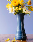 A Leland Blue Step Vase holds a bouquet of bright yellow flowers.