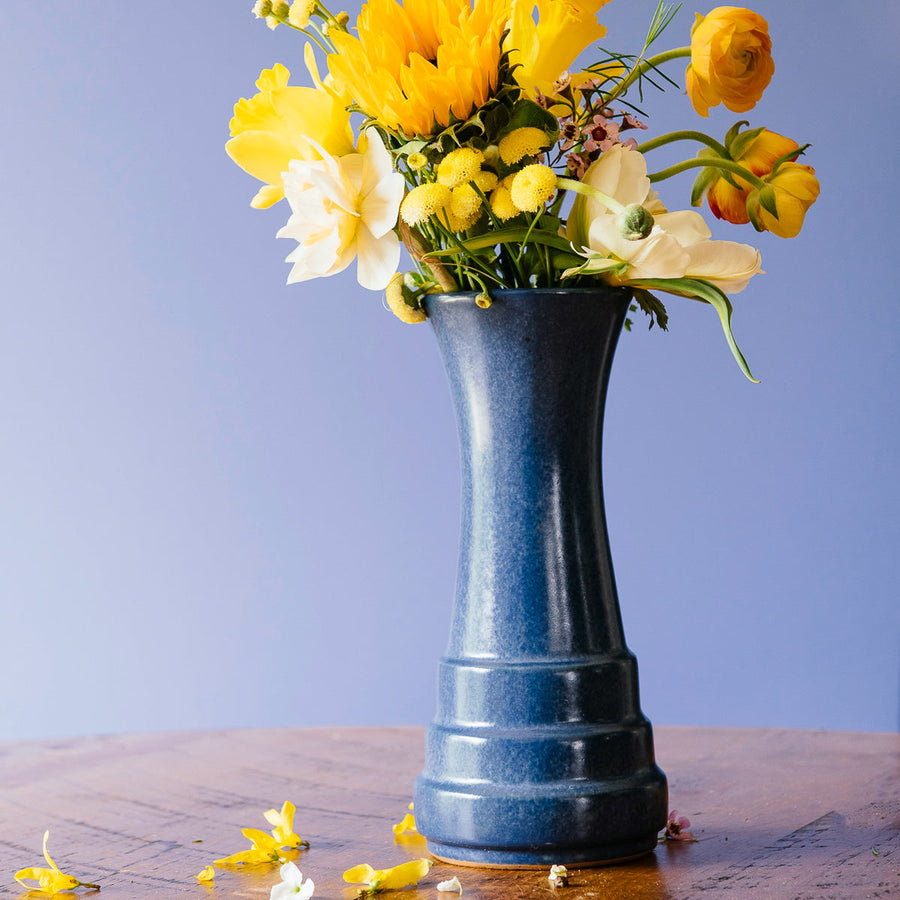 A Leland Blue Step Vase holds a bouquet of bright yellow flowers.