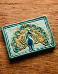 The Peacock Tile features a peacock facing straight ahead with its feathers fanned out showing off its colorful plumes. In the bottom right corner of the tile are the letters "M C S" in black writing. This is the only tile on which Pewabic's co-founder Mary Chase Stratton included a signature. The hand painted tile features bright blues, greens and beiges.