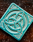 The Trinity Knot tile features a three-pointed Celtic knot interwoven with a circular ring. This knot is surrounded by a thick border with smaller three-pointed knots in each corner.