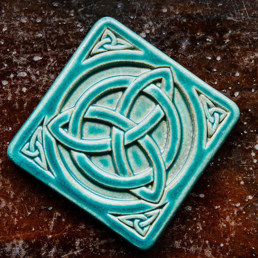 The Trinity Knot tile features a three-pointed Celtic knot interwoven with a circular ring. This knot is surrounded by a thick border with smaller three-pointed knots in each corner.