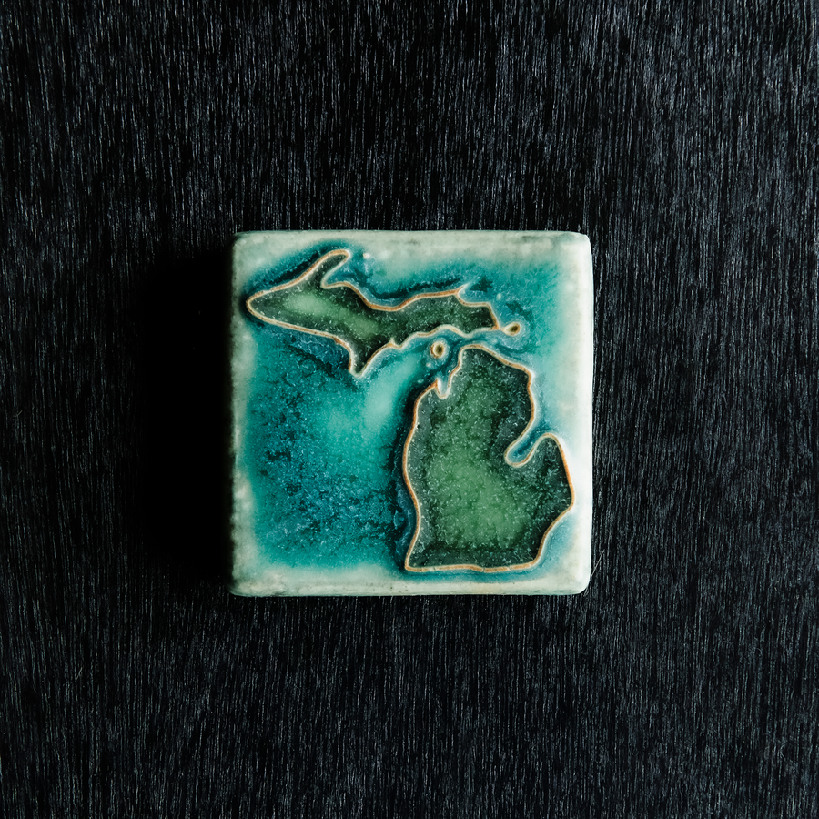 This hand painted tile has a matte turquoise background with matte earthy green peninsulas.