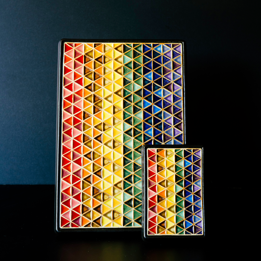 Both sizes of the Pride Tile sit next to each other. The much larger tile features more lines of interwoven triangles than the smaller version. But they have the same glaze colors and triangle pattern.