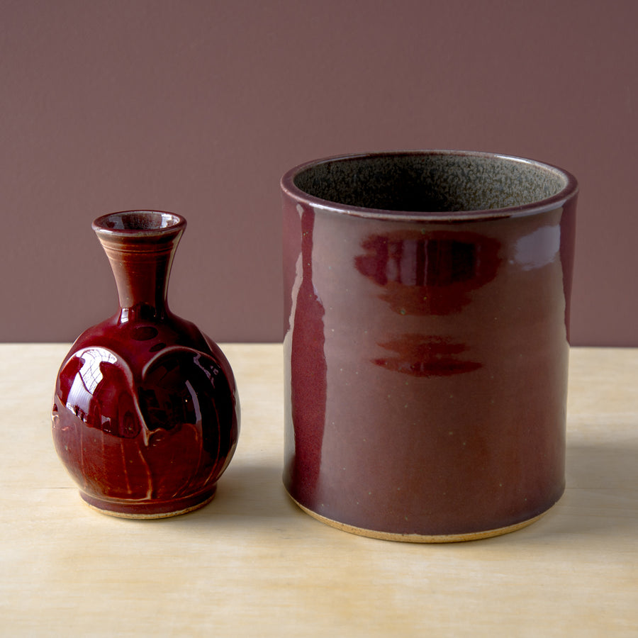 Our Merlot Crock is photographed to the right of a Classic Bud Vase in our high-gloss and more vibrant Winterberry glaze.