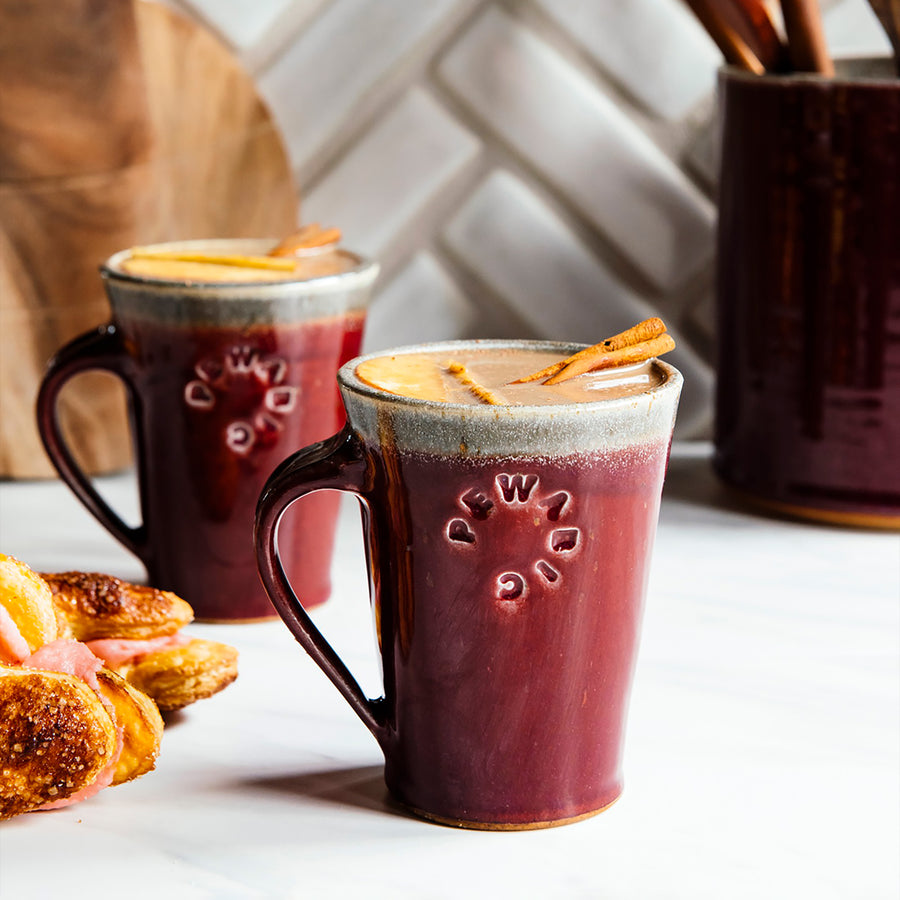 Cafe Mugs have a simple, modern design with smooth, straight sides that slant out. This makes the base slightly smaller than the cup's opening. The round Pewabic logo is stamped onto the side.
