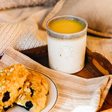 These Rocks cups feature the creamy white Birch glaze that has some brown speckling. The inner lining and lip of the cup have a mottled gray color. A Rocks cup filled with orange juice sits next to a plate covered in scones.