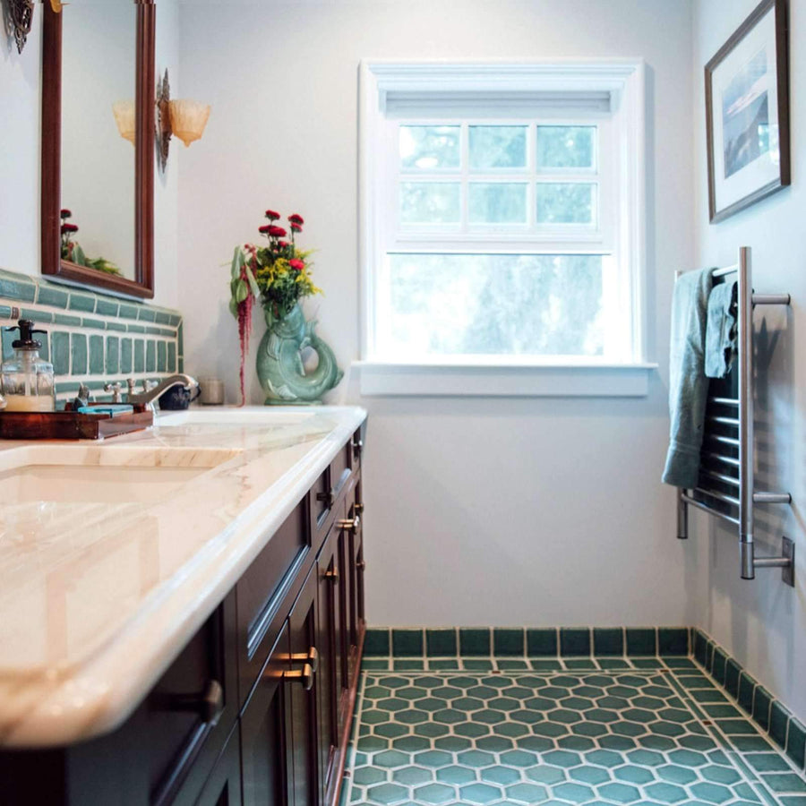 Bright white walls and a large window showcase the soft green of the tile. While the dark wood cabinets and mirror frames give a cozy look.